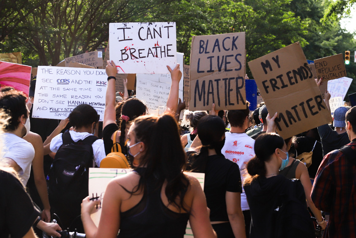 protesters with their backs against the camera, holding signs with messages supporting Black Lives Matter