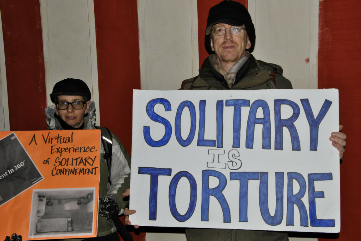 A man holding a sign that says "Solitary Is Torture"